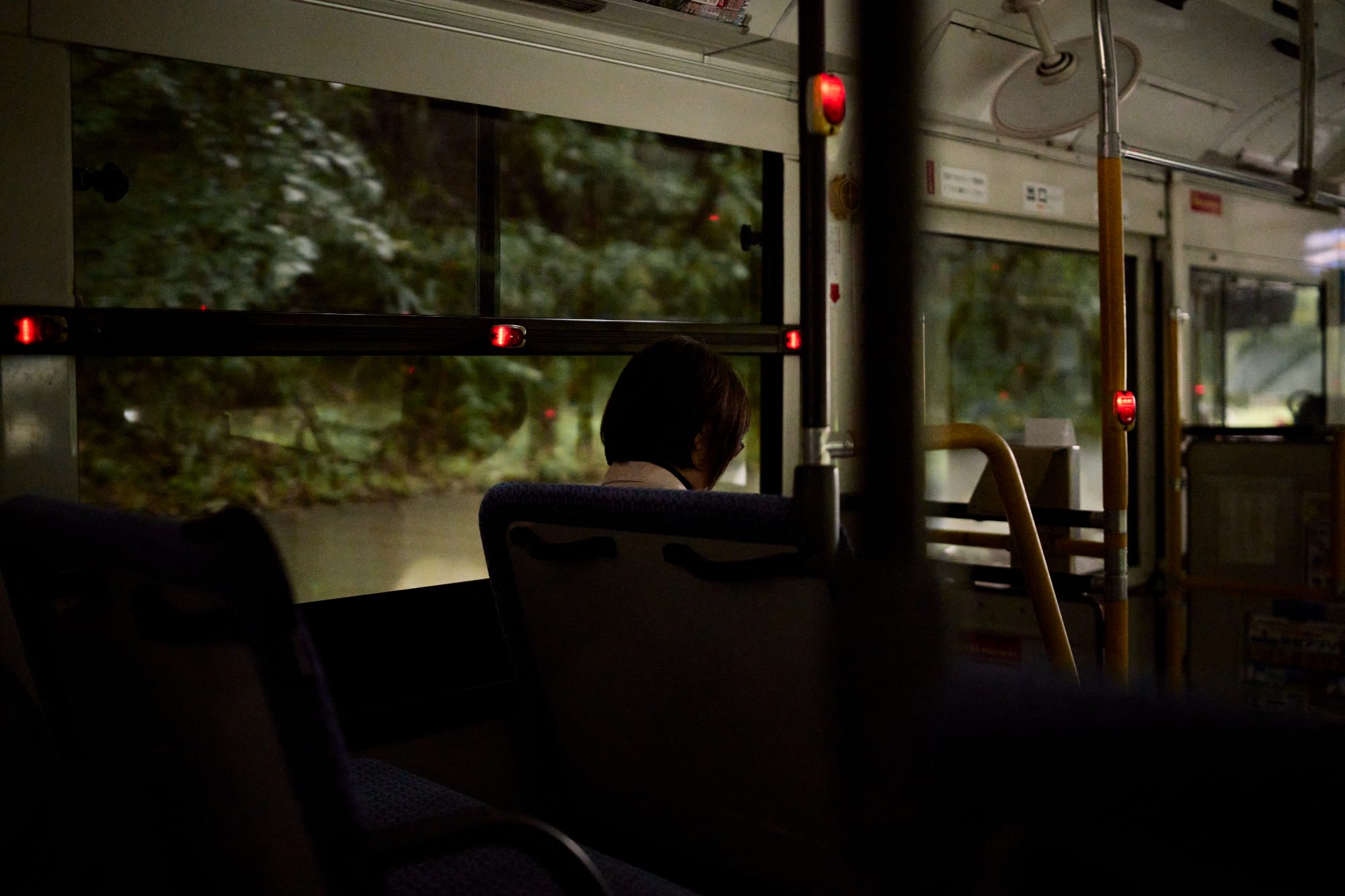 The dim interior of a city bus, a passenger silhouetted against the rain-streaked window