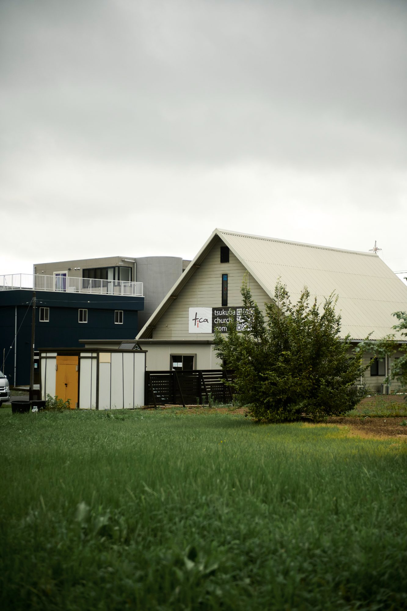 A dark blue house with a steep white roof beside a mown green field