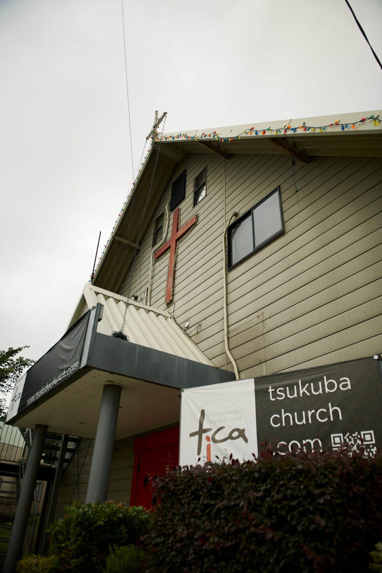 The TICA Tsukuba church building with a red cross on its wall under a grey sky