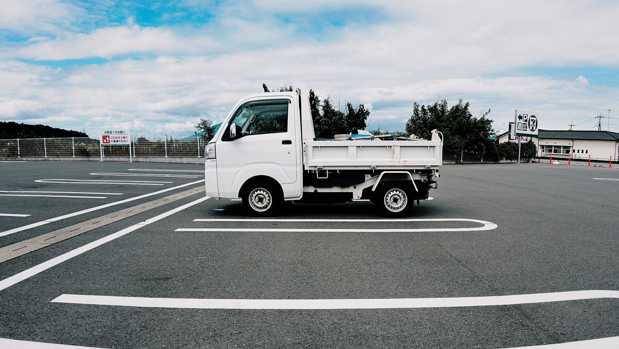 A white kei truck parked in an empty lot under blue sky