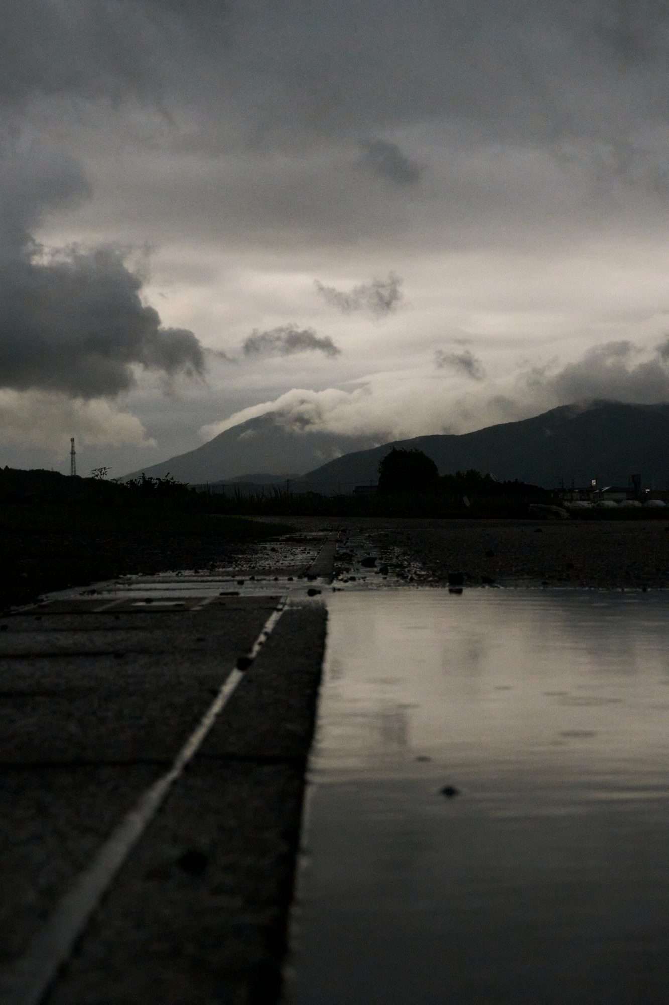A wet road at dusk with a dark mountain under heavy clouds