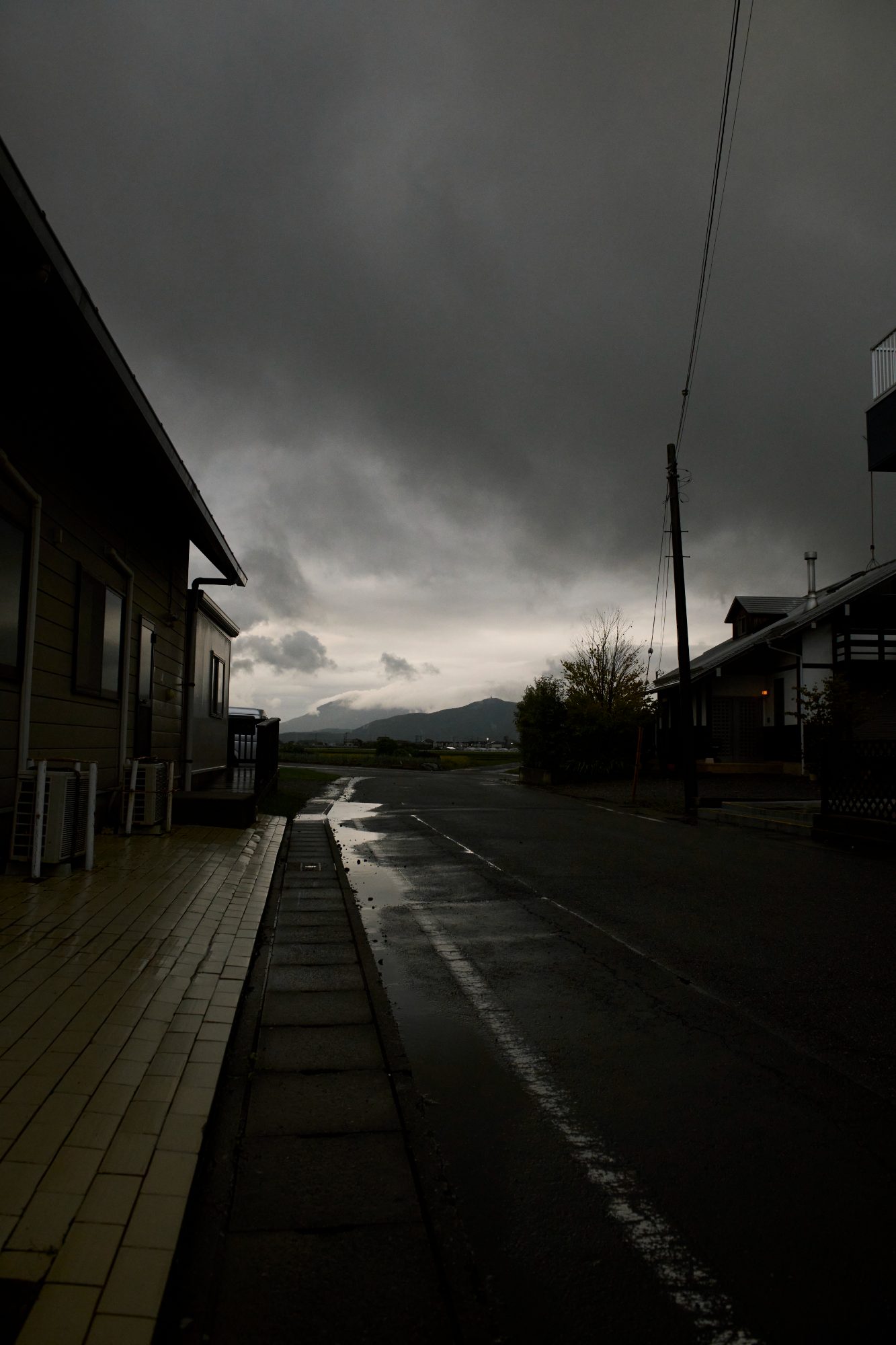 A dark street beside a long low building, sky glowing at the end