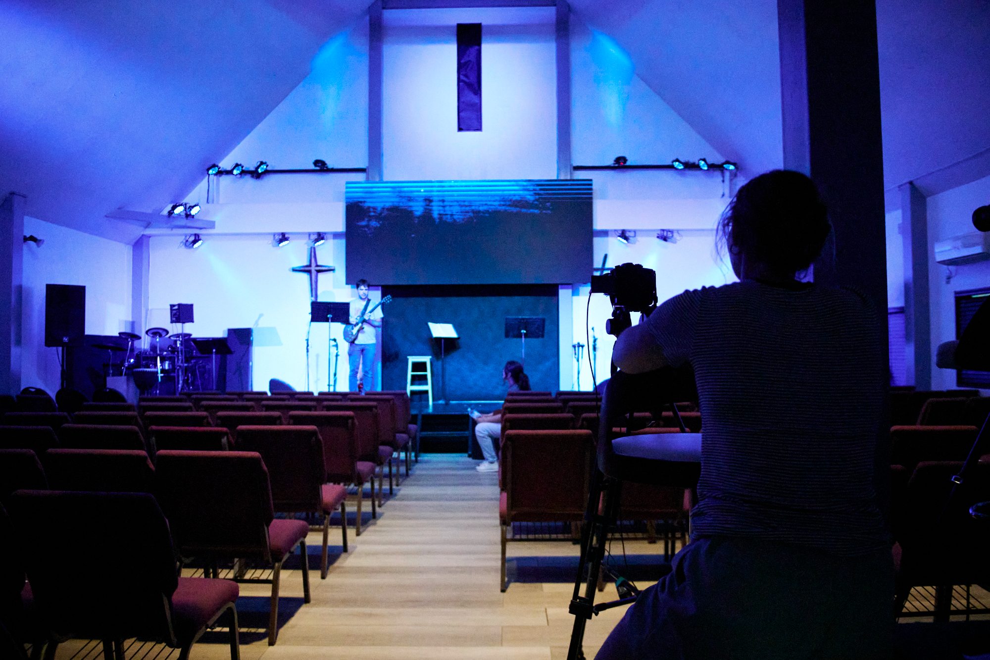 A church sanctuary lit in blue during a Sunday service, seen from the back rows