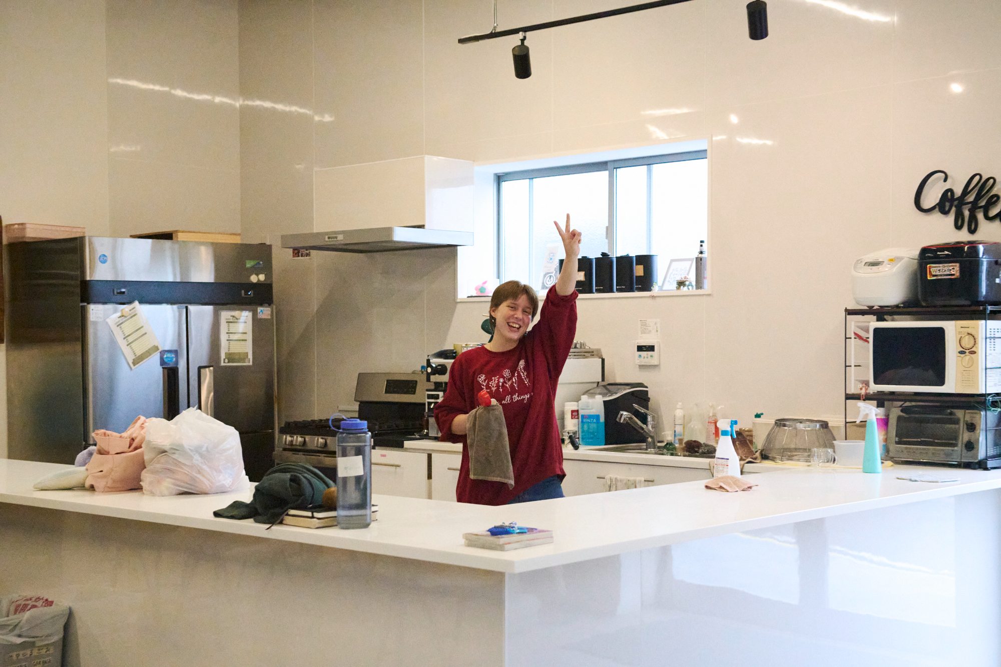 A bright café kitchen with someone waving from behind the counter