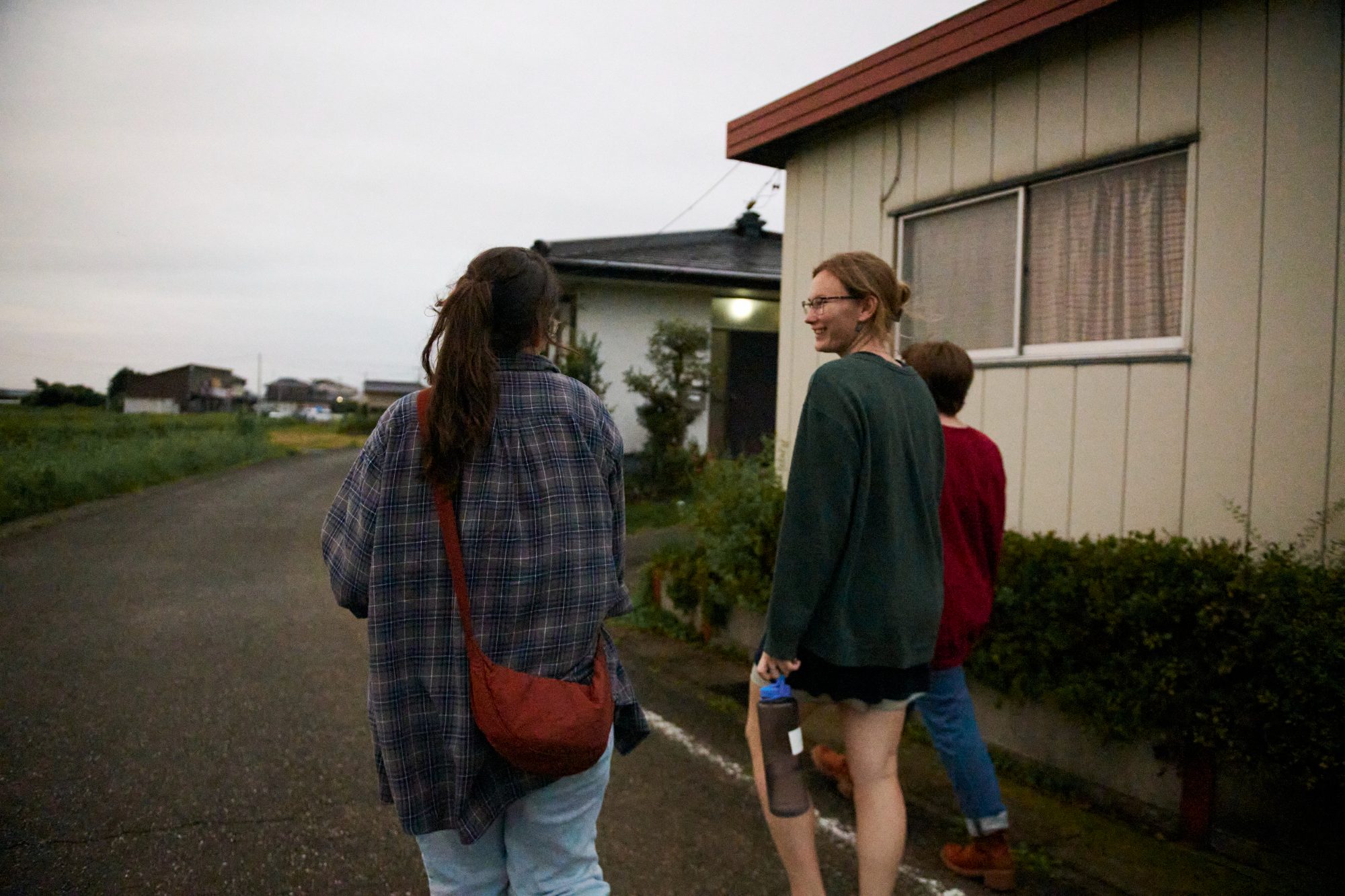 Two people walking past a grey house, heading down the lane