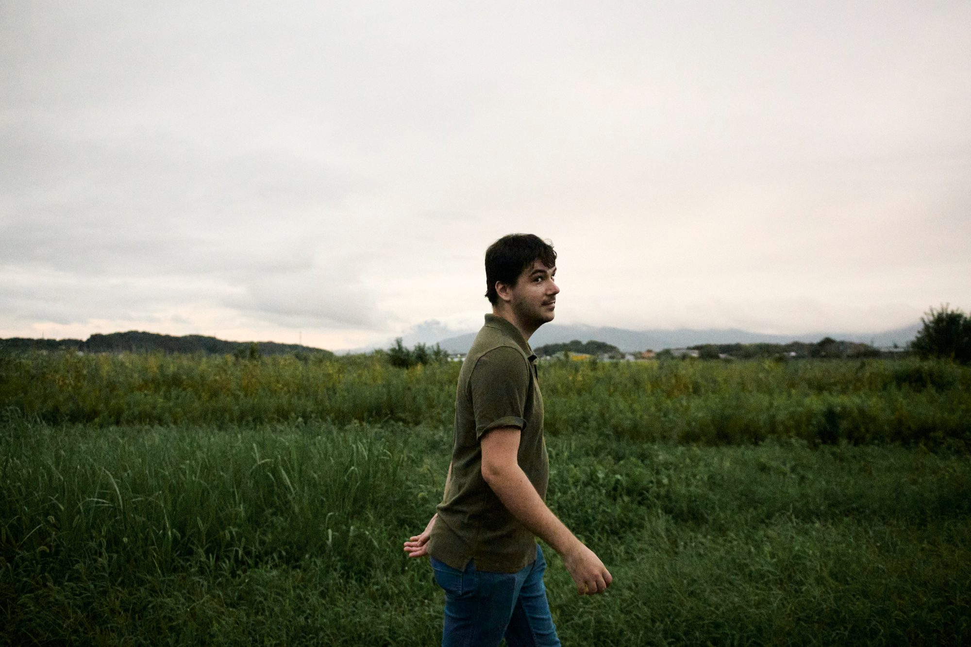 A man standing in tall green grass, looking off toward the horizon
