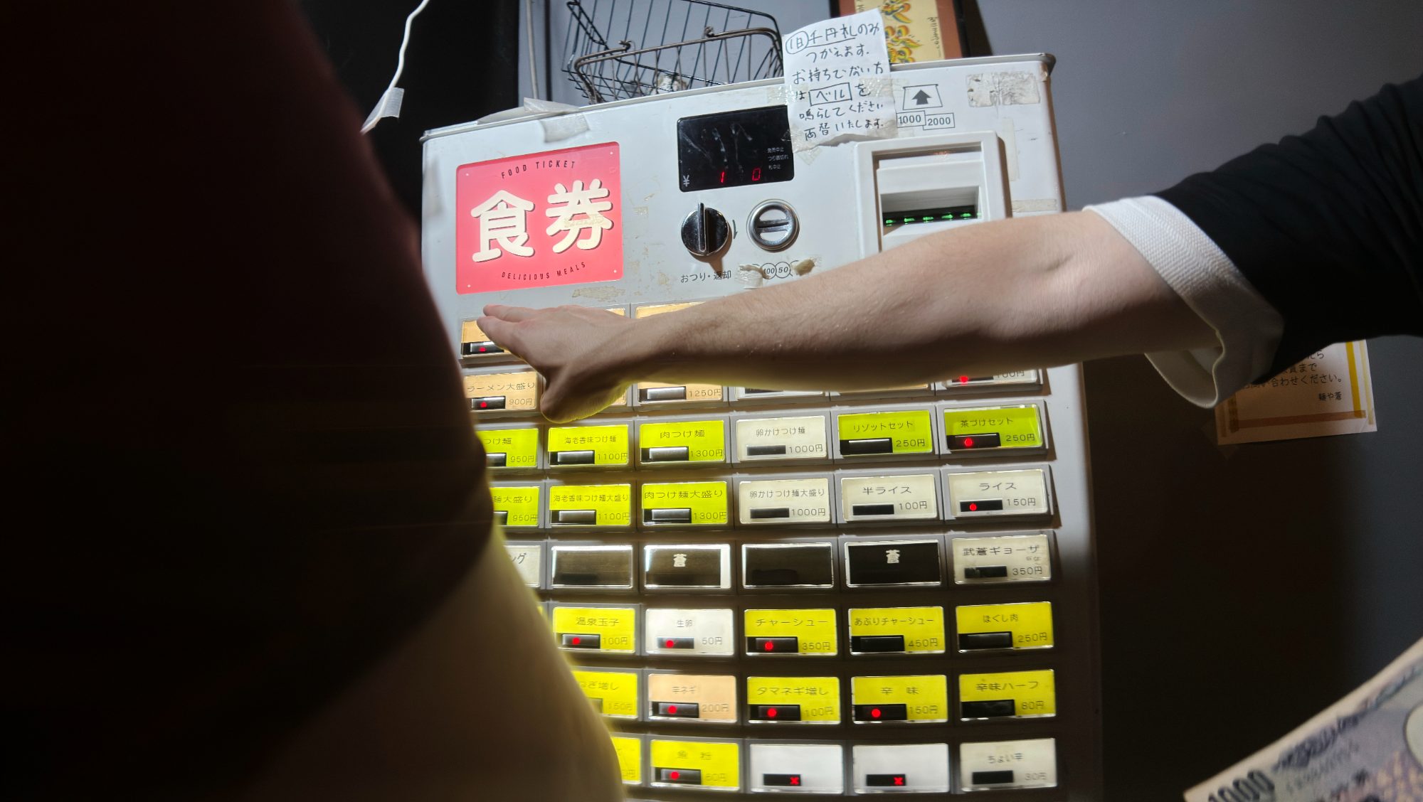 A hand pressing a button on a Japanese meal ticket machine
