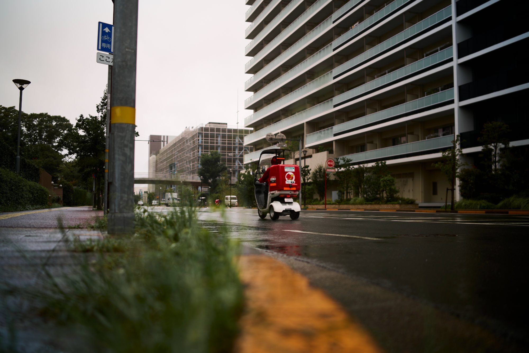 A red scooter passing a wet street with grass in the foreground