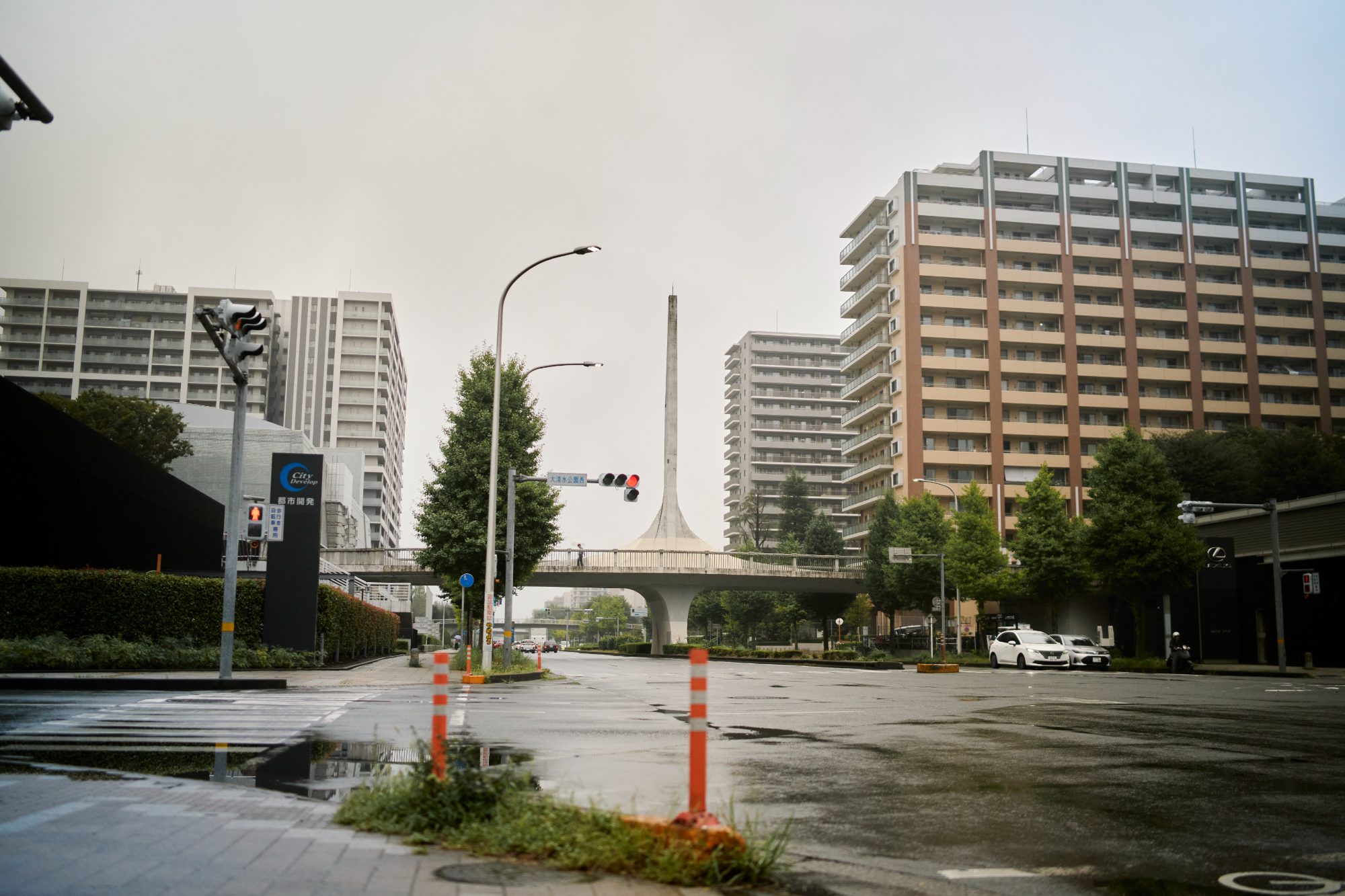 A wide, wet city intersection with apartment towers under grey sky
