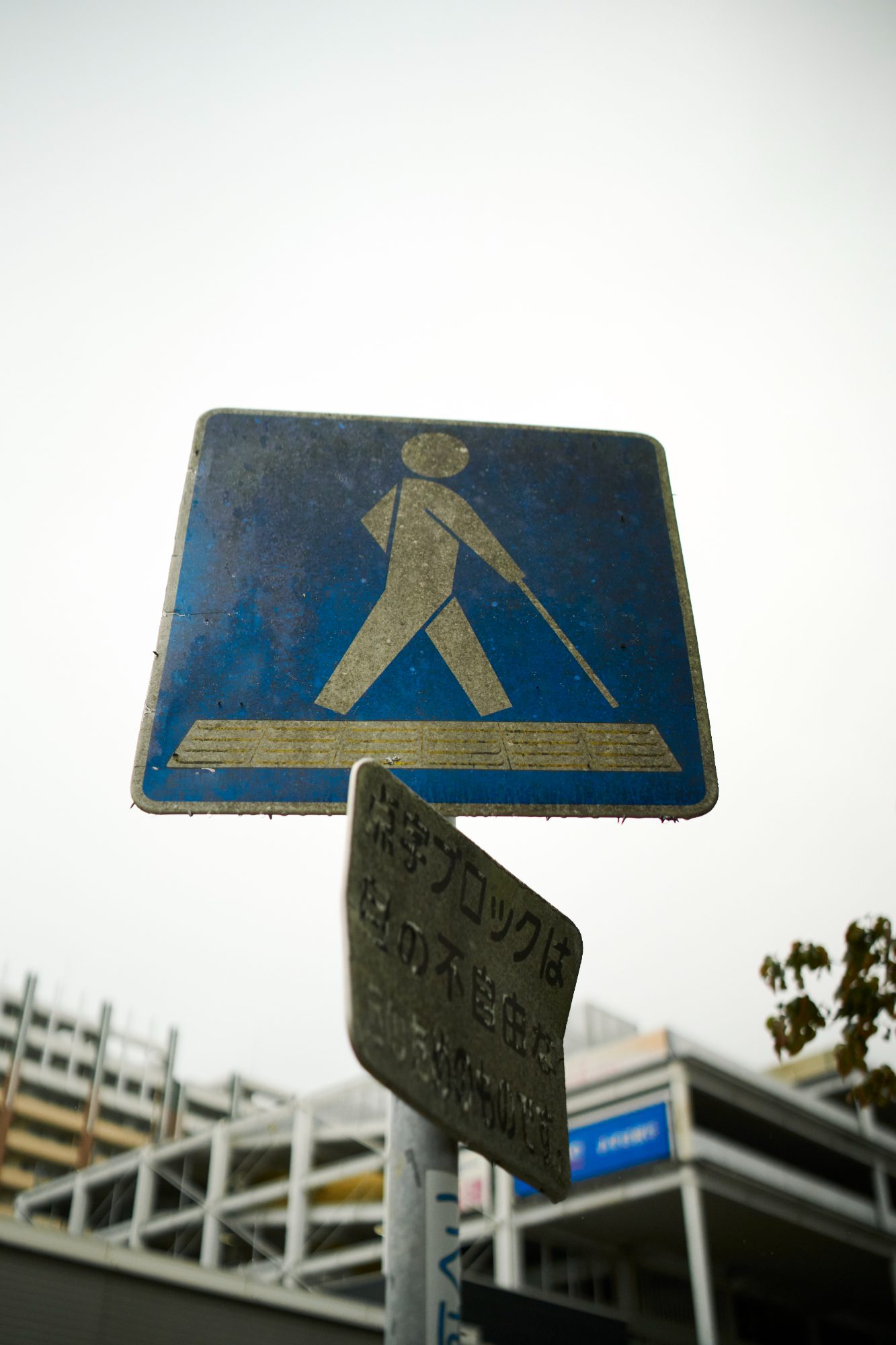 A weathered blue pedestrian crossing sign against a bright sky