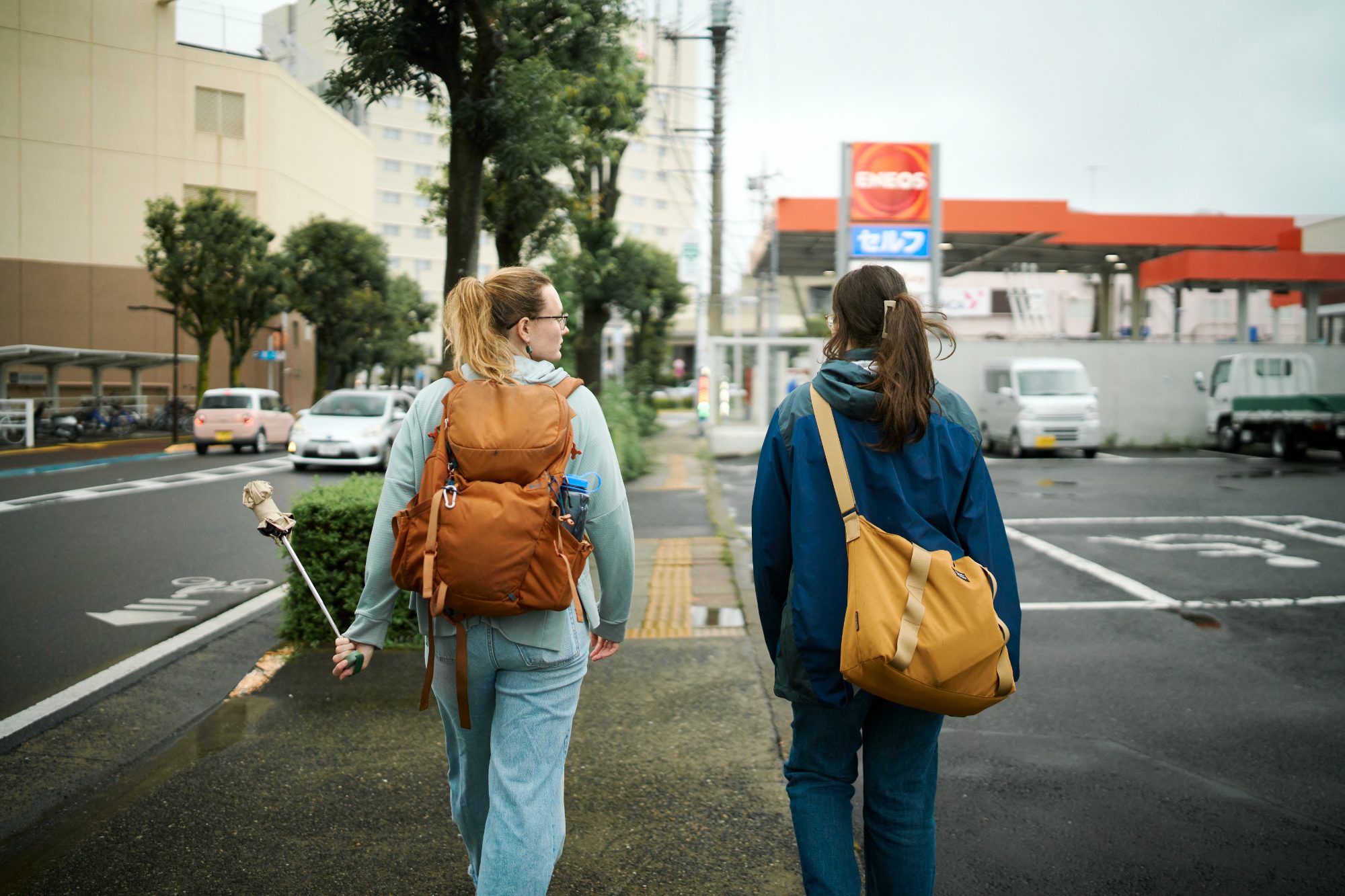 Two travelers with backpacks crossing a city street on a rainy day
