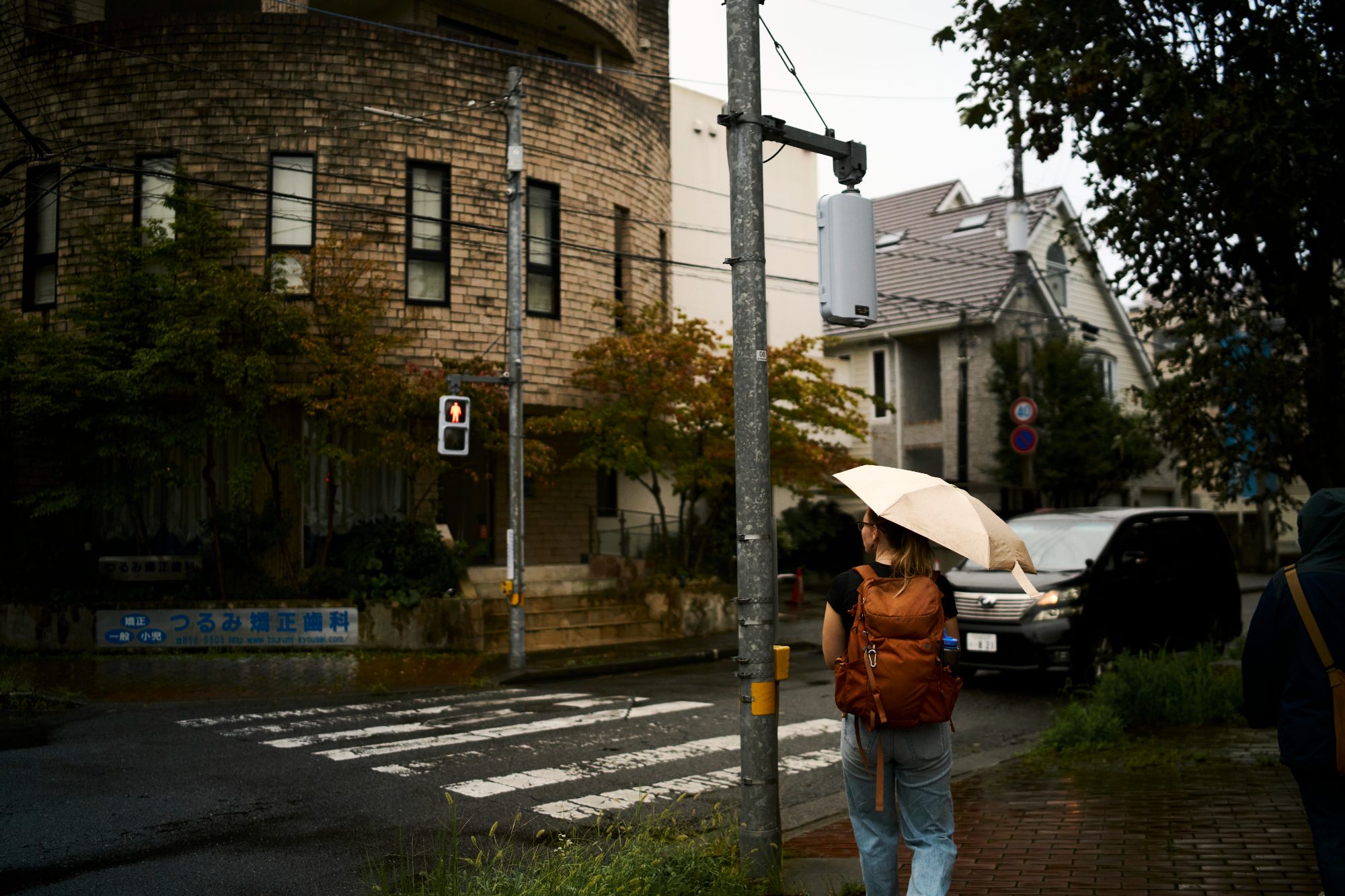 A person with an umbrella crossing at a corner beside a brick building