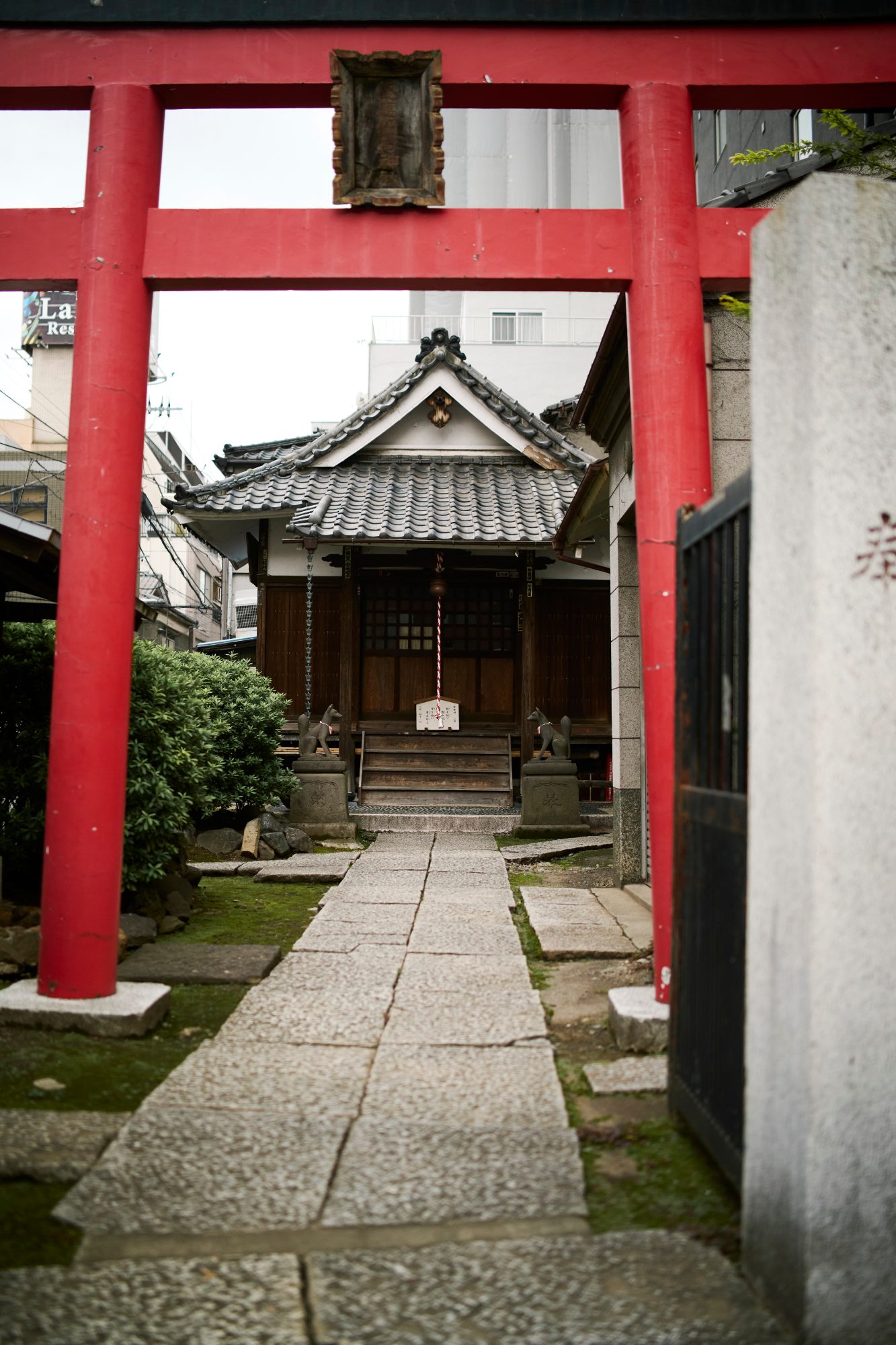 A red torii gate framing a small neighborhood shrine