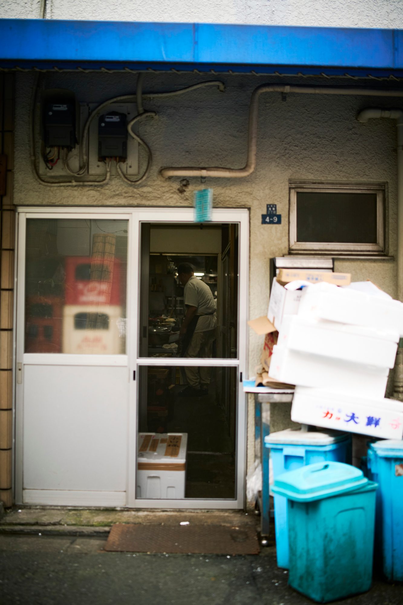 A white door beneath a blue awning, crates stacked beside it