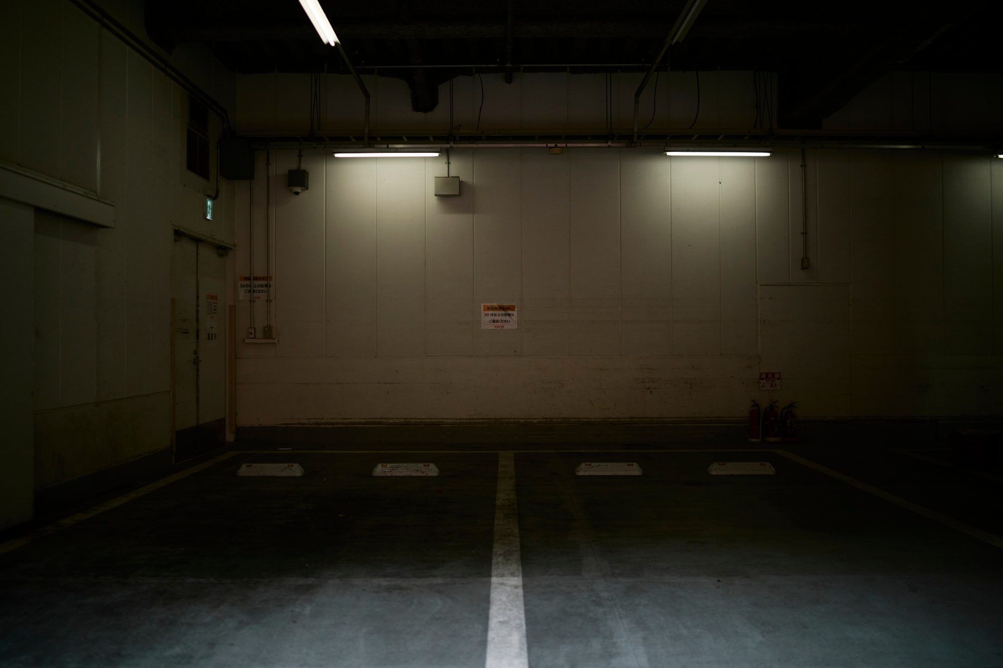 An empty underground parking garage lit by fluorescent tubes