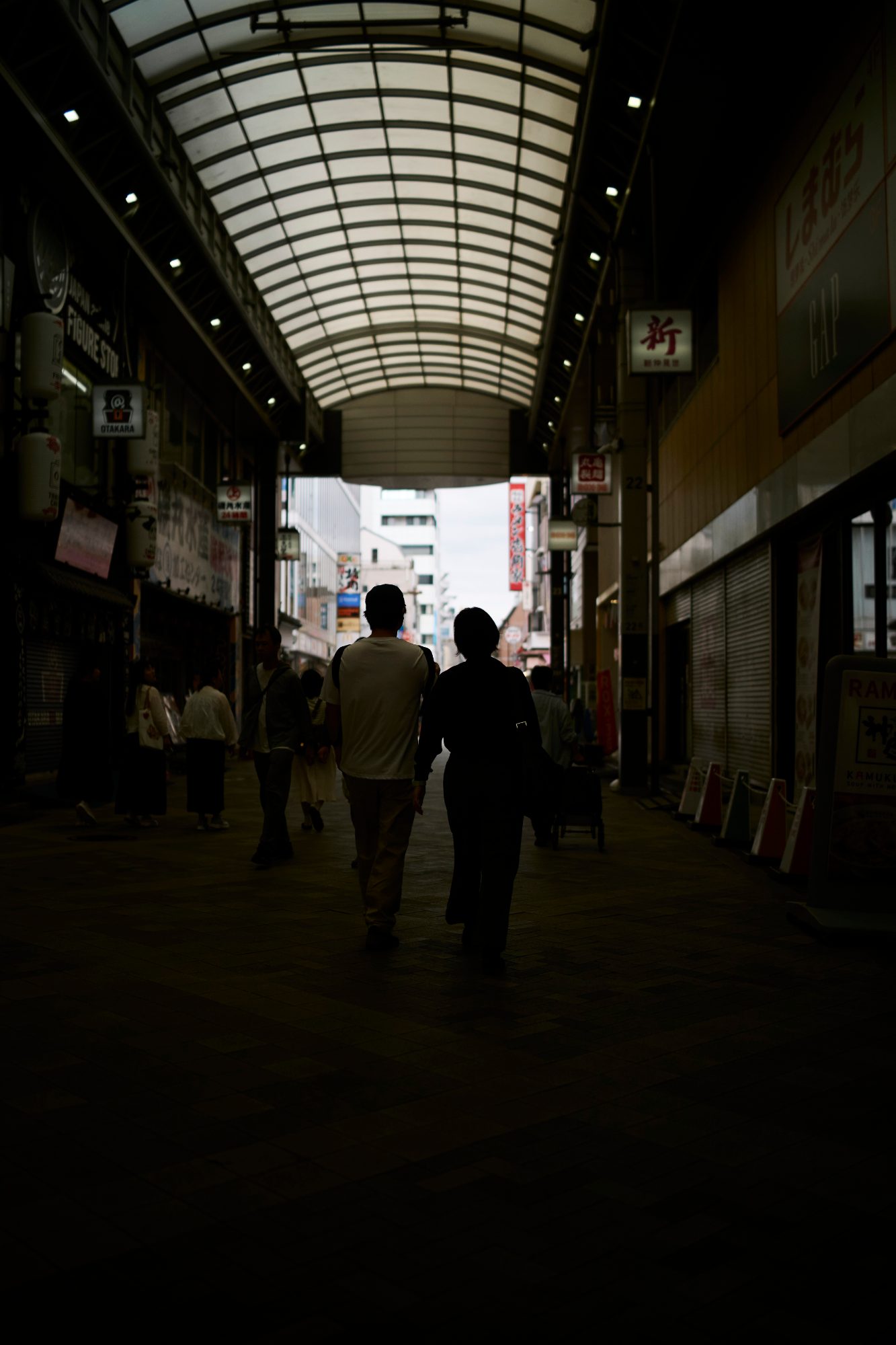 Silhouettes walking through a dim covered arcade