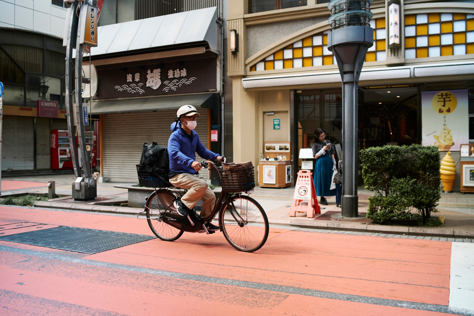 A man cycling past a shopping street on a red-paved road