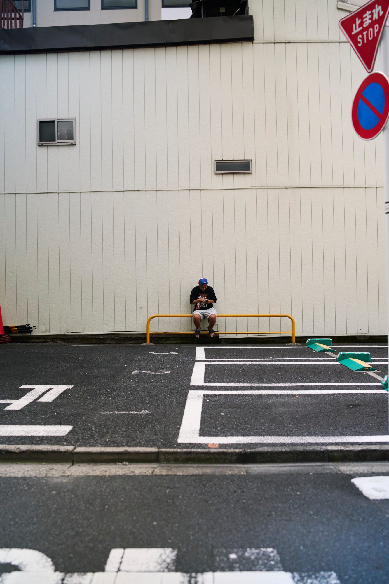 A man sitting alone at the edge of a small parking lot