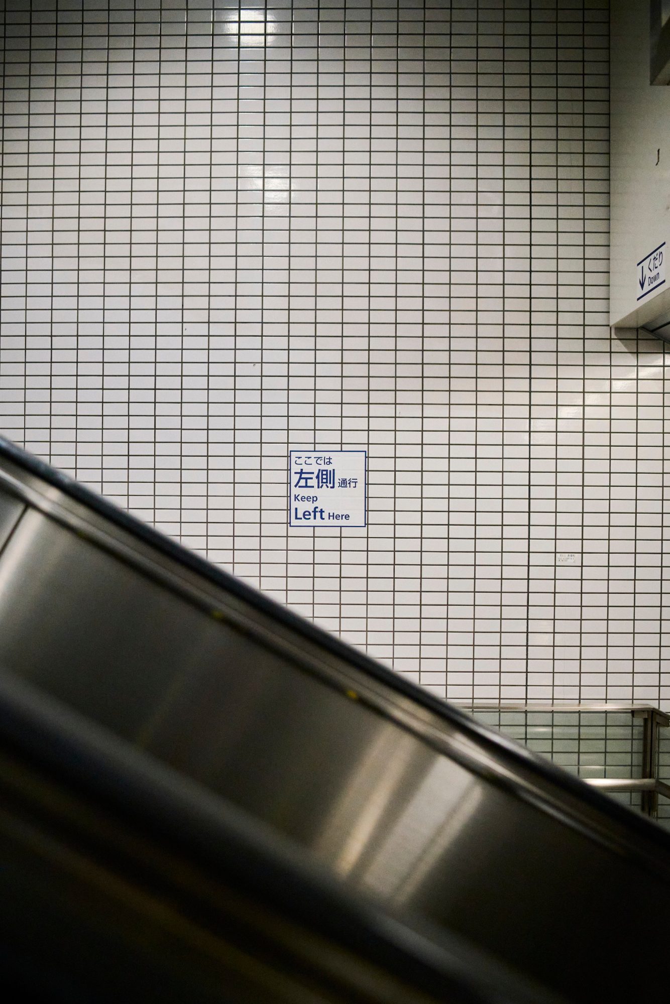 White tiled wall beside an escalator handrail
