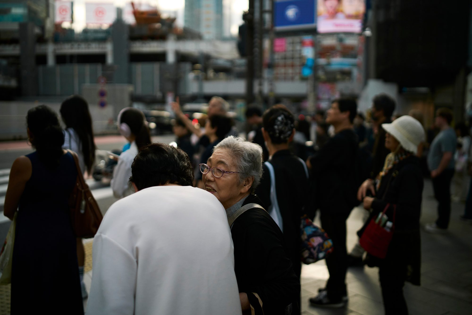 A crowd waiting to cross, an older woman turning toward the camera