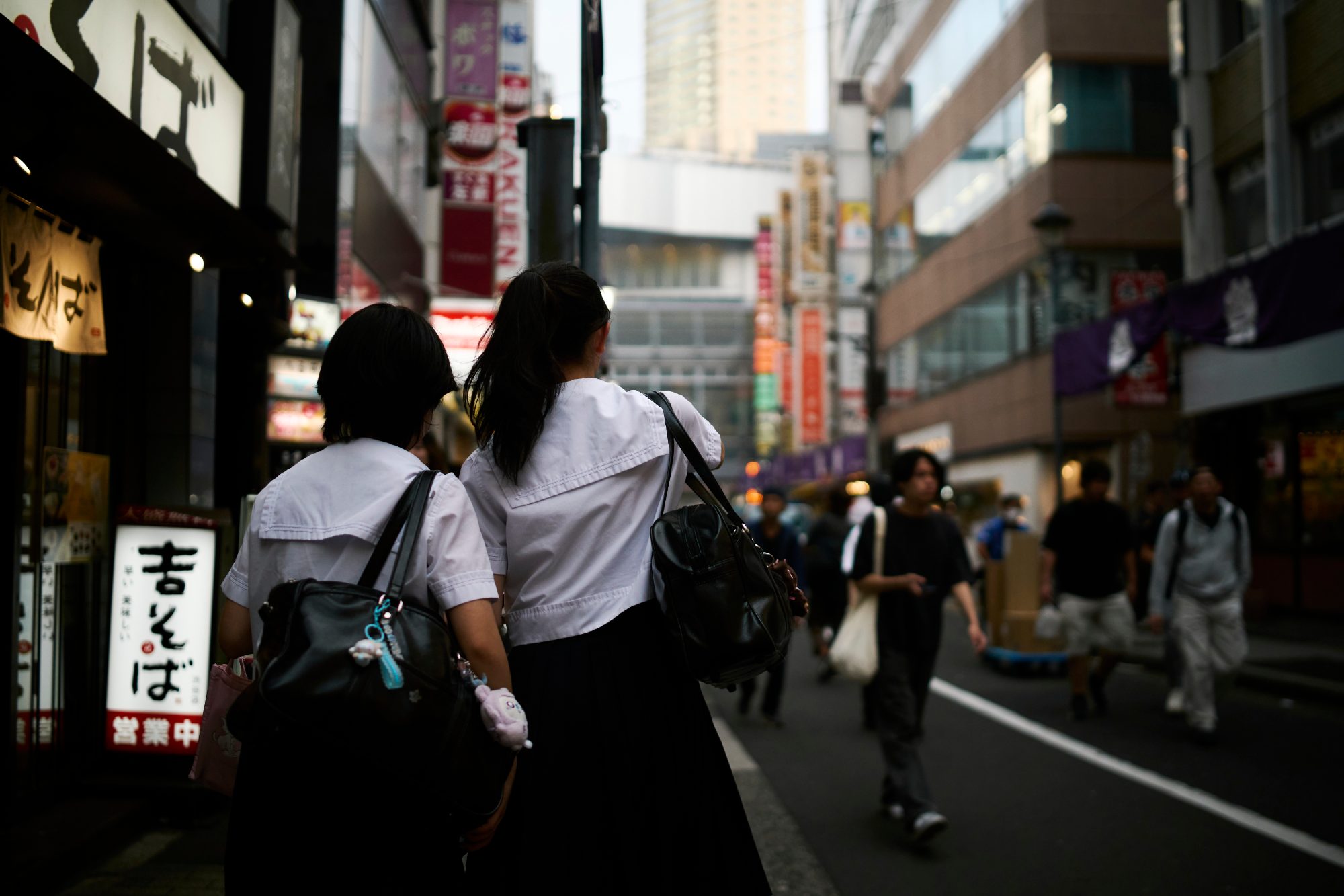 Shoppers crossing a neon-lit street in the evening