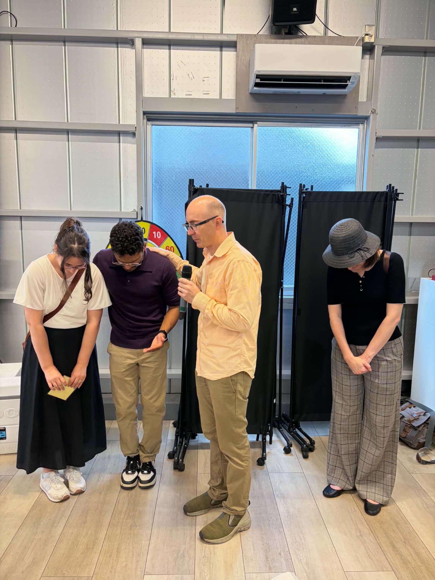 The church praying over Kelly and Luis, heads bowed, as the pastor speaks into a microphone