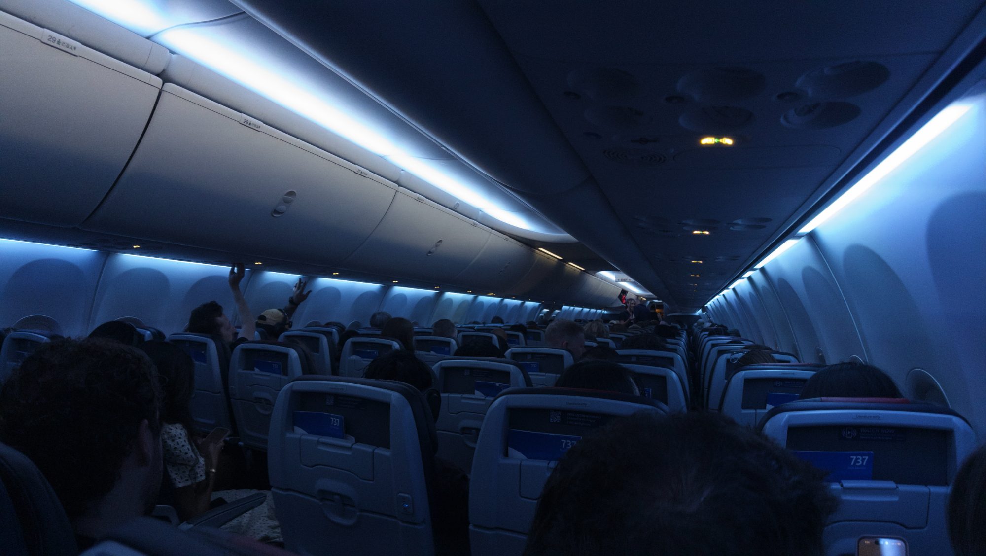 Airplane cabin lit blue, passengers settling in for a long flight