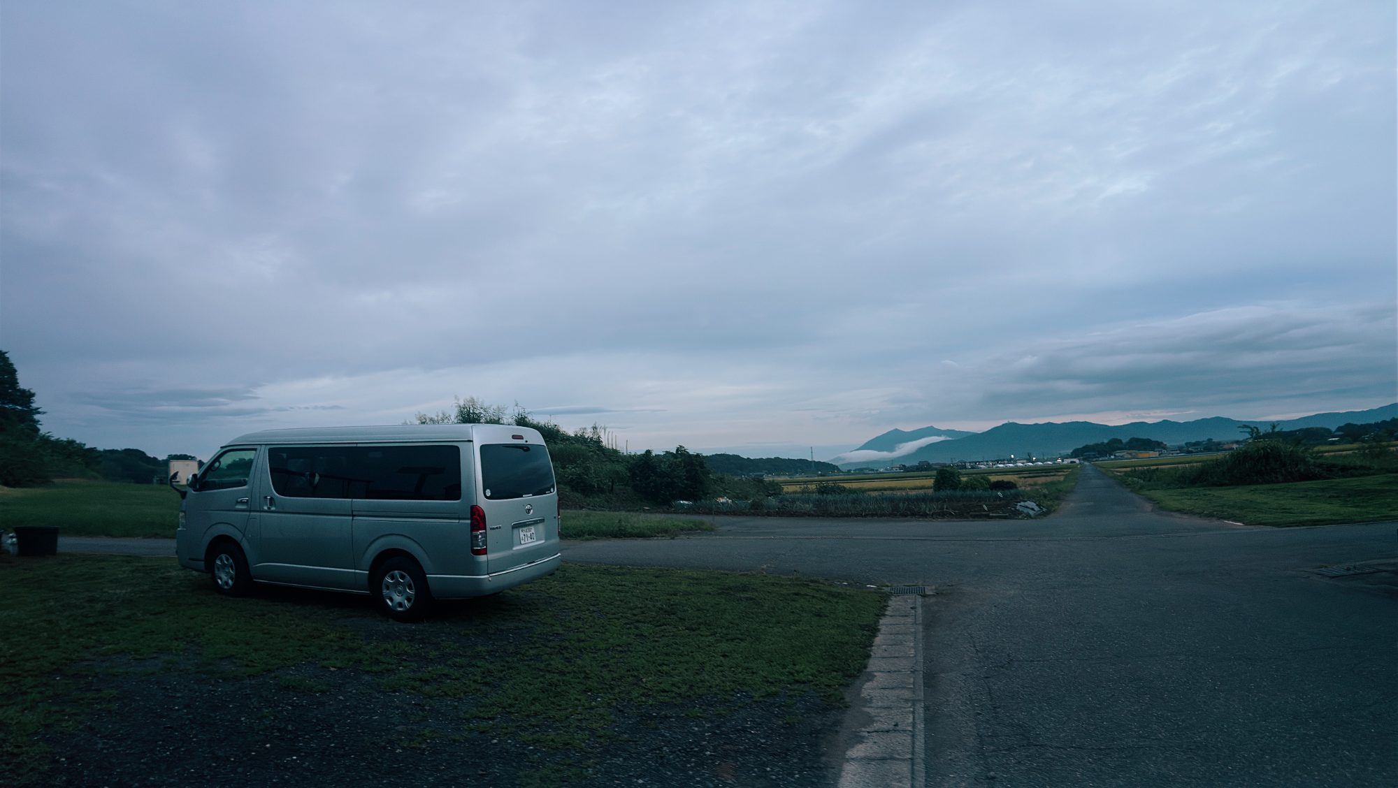 A white van parked at the edge of fields with mountains in the distance at dusk
